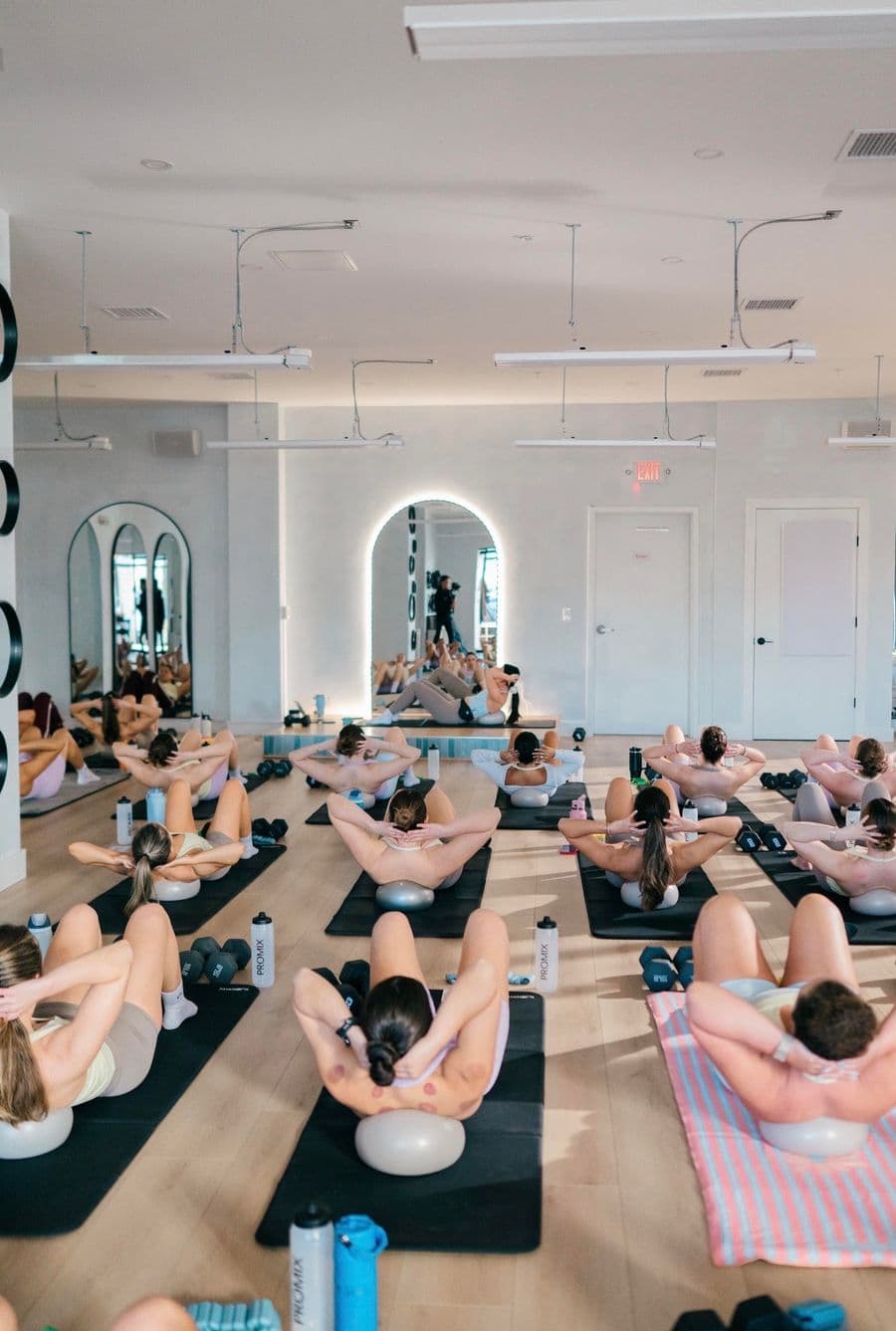 Participants performing a low-impact Sculpt workout with dumbbells during a group fitness class at a Boston studio.